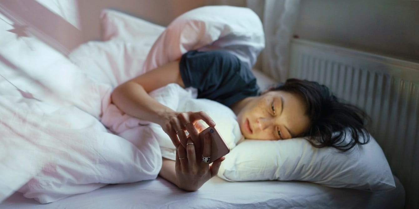 Constantly doomscrolling? An expert shares how to avoid the rabbit holes woman laying in bed on her phone - how to stop doomscrolling
