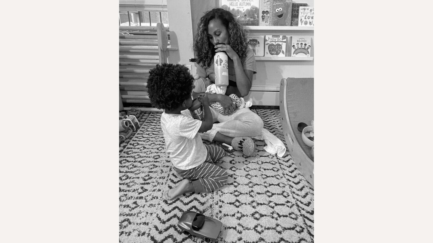 The transition to becoming a mom of two is beautiful—but also hard mother sitting on floor holding baby with toddler in front of her