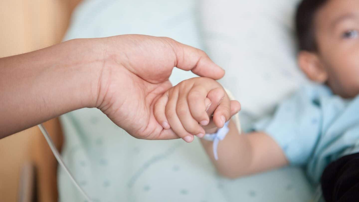 No kid should have to face cancer. But, if they do, a new initiative led by a nonprofit can help them not just survive but thrive mom holding baby's hand in hospital - Motherly's partnership with the Dare to Dream Project