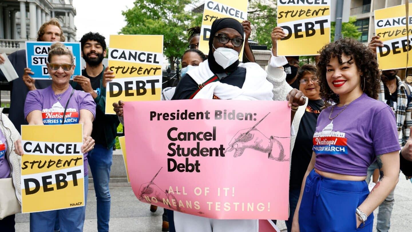 Biden cancels $10,000 in student debt for borrowers earning less than $125,000 and extends payment pause people holding signs about canceling student debt at a protest