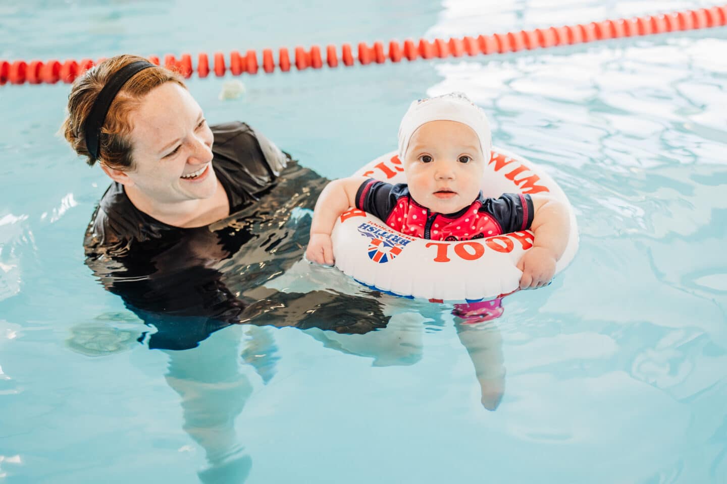 What are survival-first swim lessons? What every parent should know! baby swimming in a tube in the pool getting assisted by a swim coach