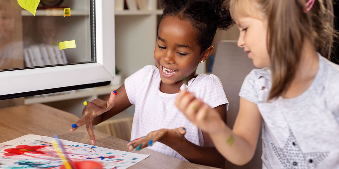 How to make finger paint—a taste-safe recipe for tiny fingers two girls sitting at a table, learning how to make finger paint