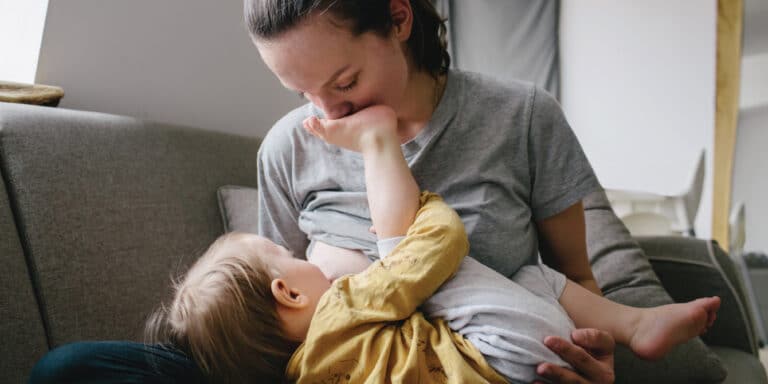 AAP recommends breastfeeding for at least 2 years. Here’s how to actually make that happen mom breastfeeding baby in the evening at home and trying to reach her extended breastfeeding goals