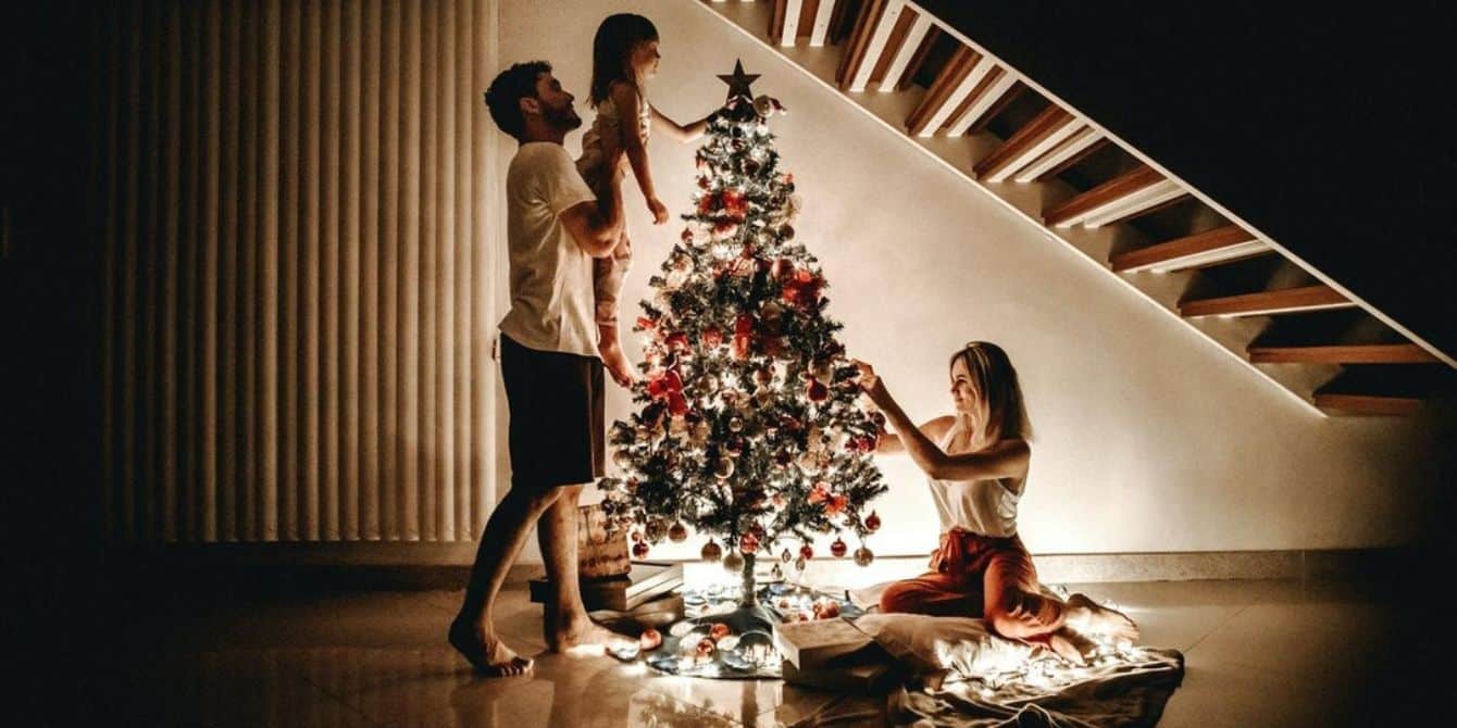 10 truly magical Christmas photo ideas for a unique and fun holiday card father picking up daughter to put star on tree and mom putting ornaments on- christmas photo ideas