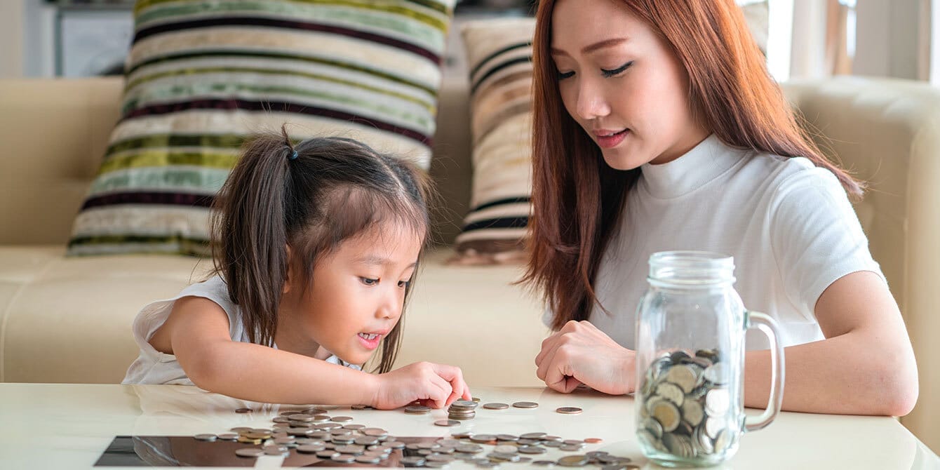 6 experts share how they teach their kids about money Mom and daughter counting coins from a jar learning about money.