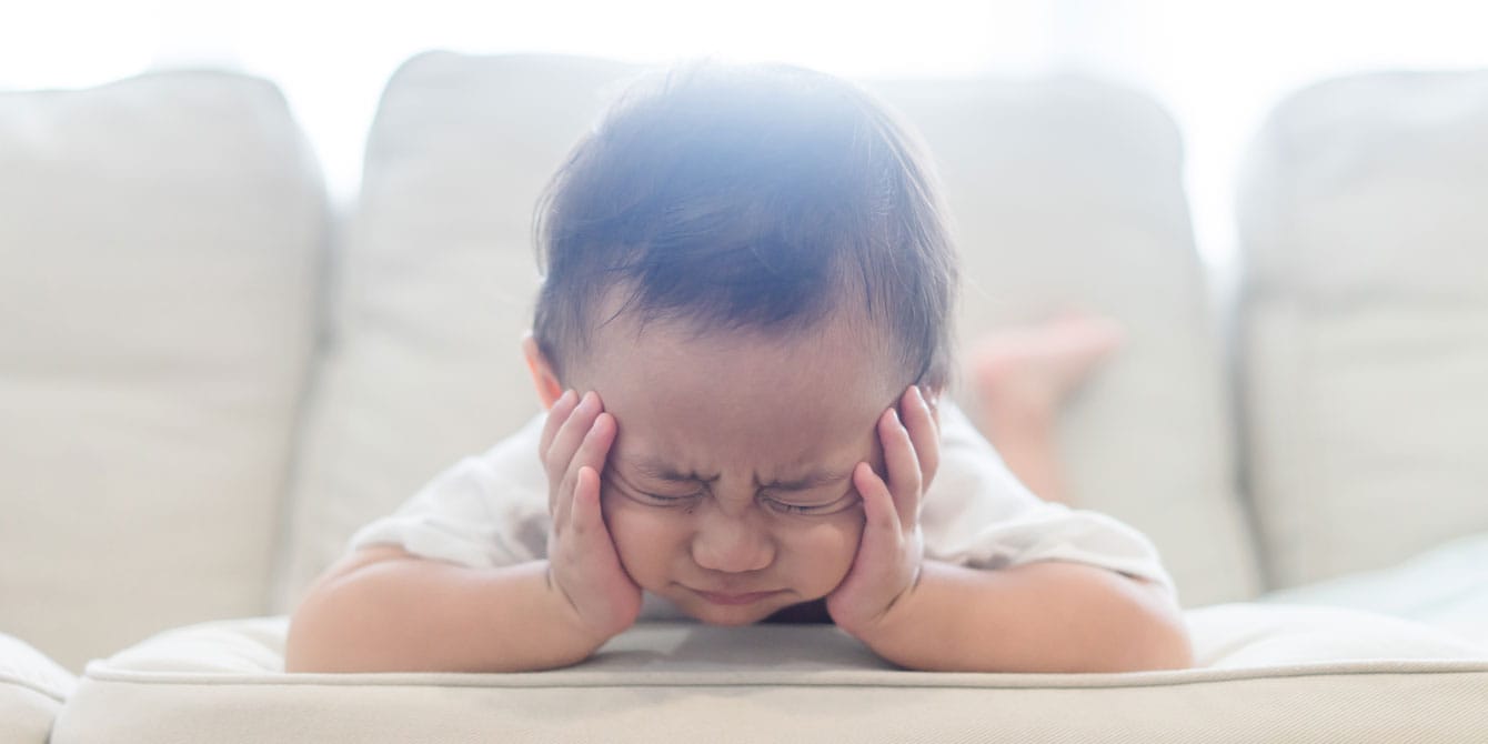 What it means when your toddler refuses to potty train, according to a pediatric urologist baby laying on couch making a grumpy face - toddler refuses to potty train