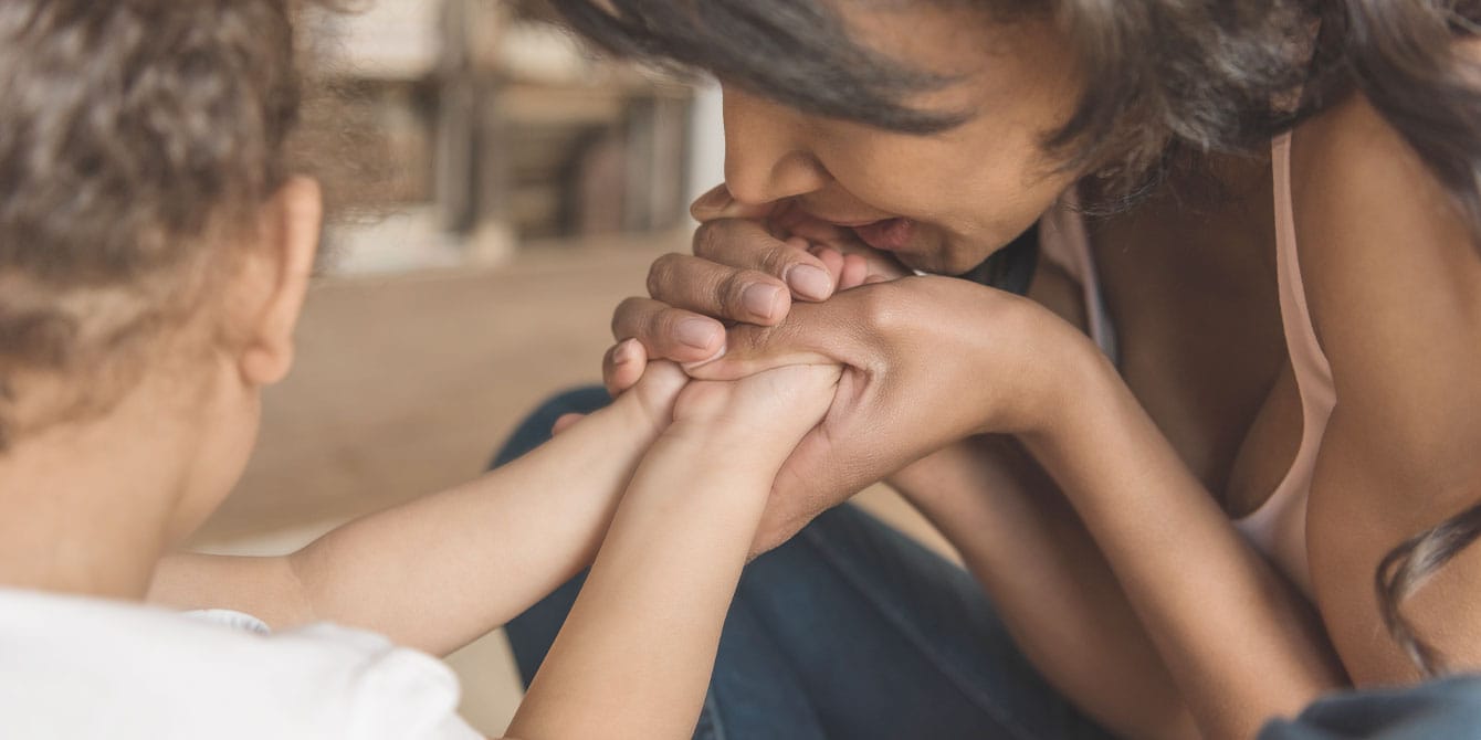 Reducing medical trauma in kids is straightforward. So why aren’t we doing it? mom kissing her baby's hands - reducing medical trauma in kids around fear of needles