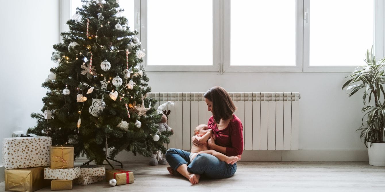 6 tips to maintain your newborn’s routine during the holiday season mother breastfeeds her baby by a Christmas tree - keeping newborn routines during holidays consistent