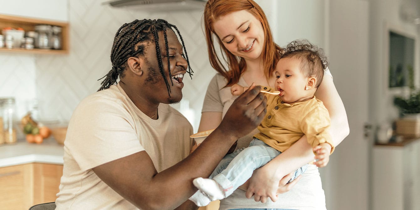 5 sustainable parenting tactics to try this year smiling mom holding baby while smiling dad feeds baby baby food