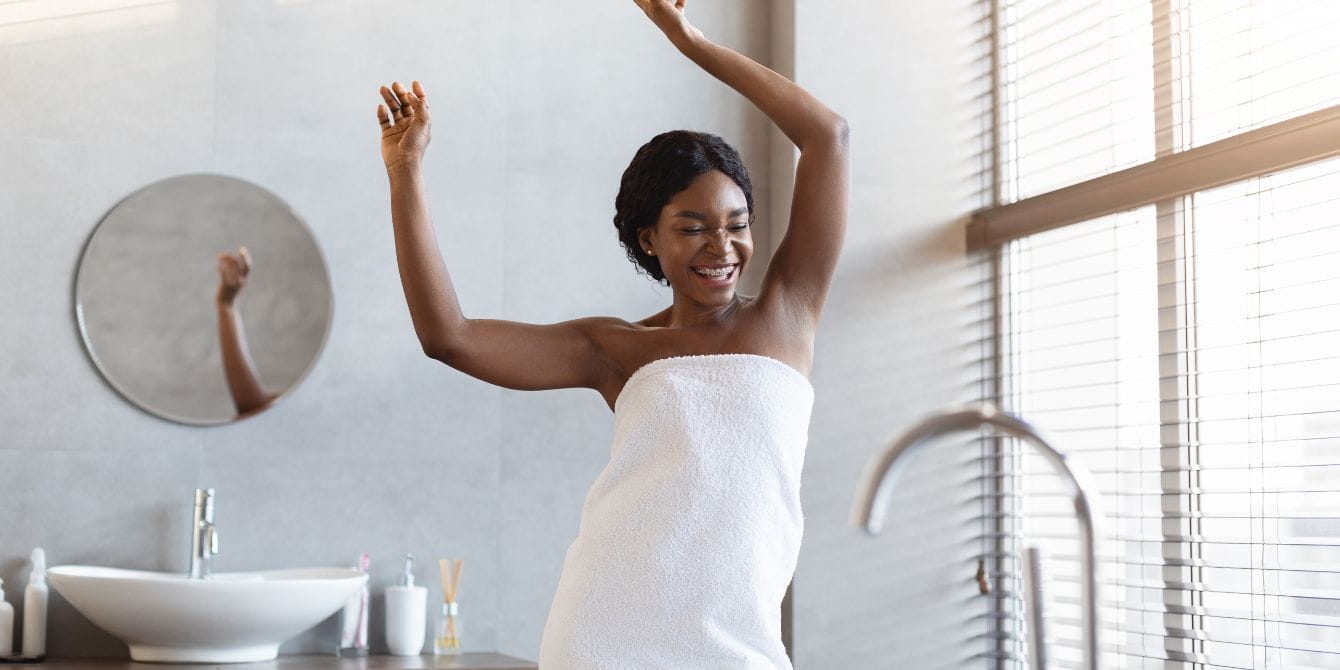 8 shower steamers that even busy moms have time to enjoy happy woman covered in white towel dancing and laughing in modern bathroom