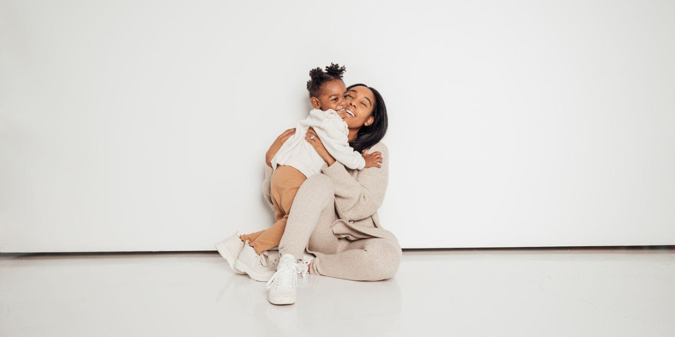 mom and daughter hugging against a white wall - Motherly