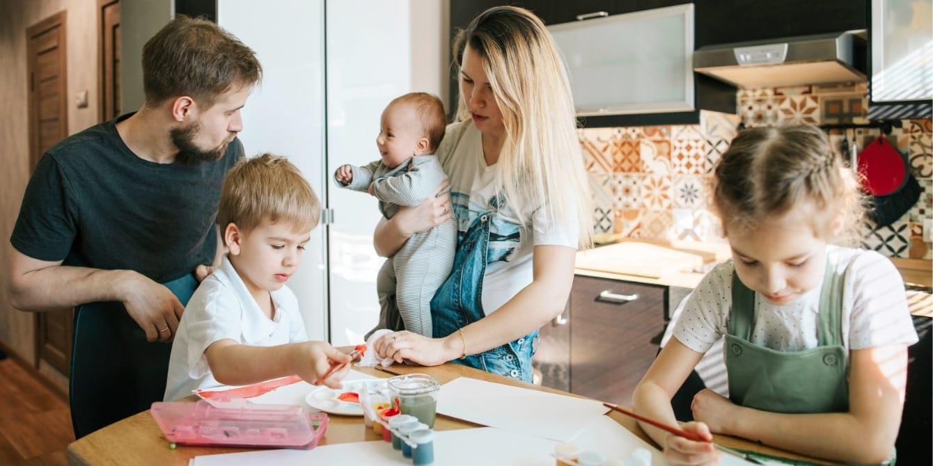 No, you don’t HAVE to book a vacation during every school break mom dad and kids hanging out in the kitchen- stay home during school vacation