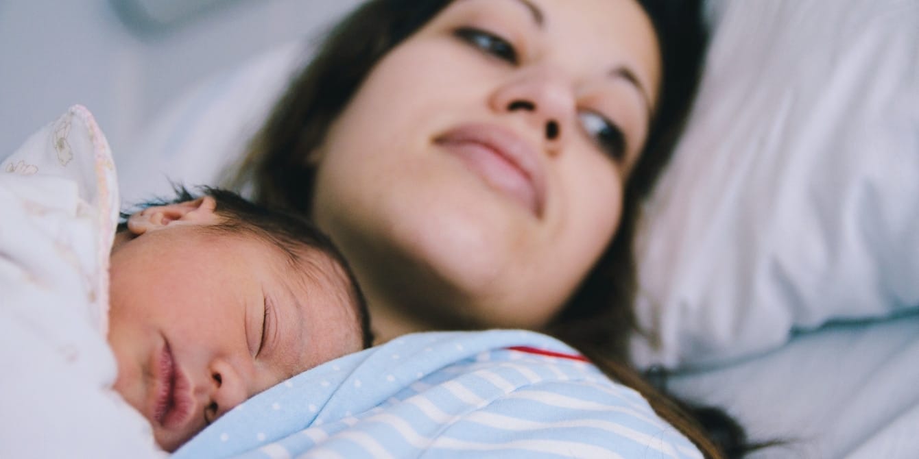 What is motherhood imposter syndrome? Here’s how to recognize it mother with her newborn baby in hospital bed - motherhood imposter syndrome