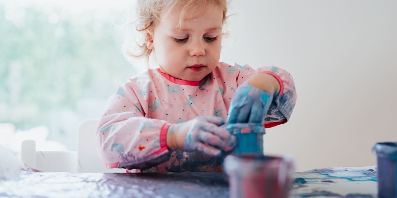 How to make homemade sustainable finger paint for kids toddler putting hand into a cup of blue fingerpaint
