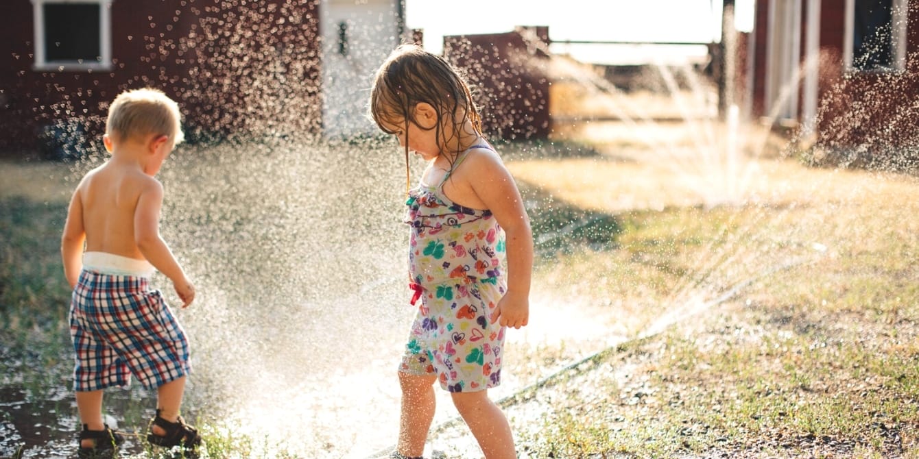 Modern parenting is exhausting—I’m giving my kids an ’80s summer kids playing on the lawn in the sprinklers