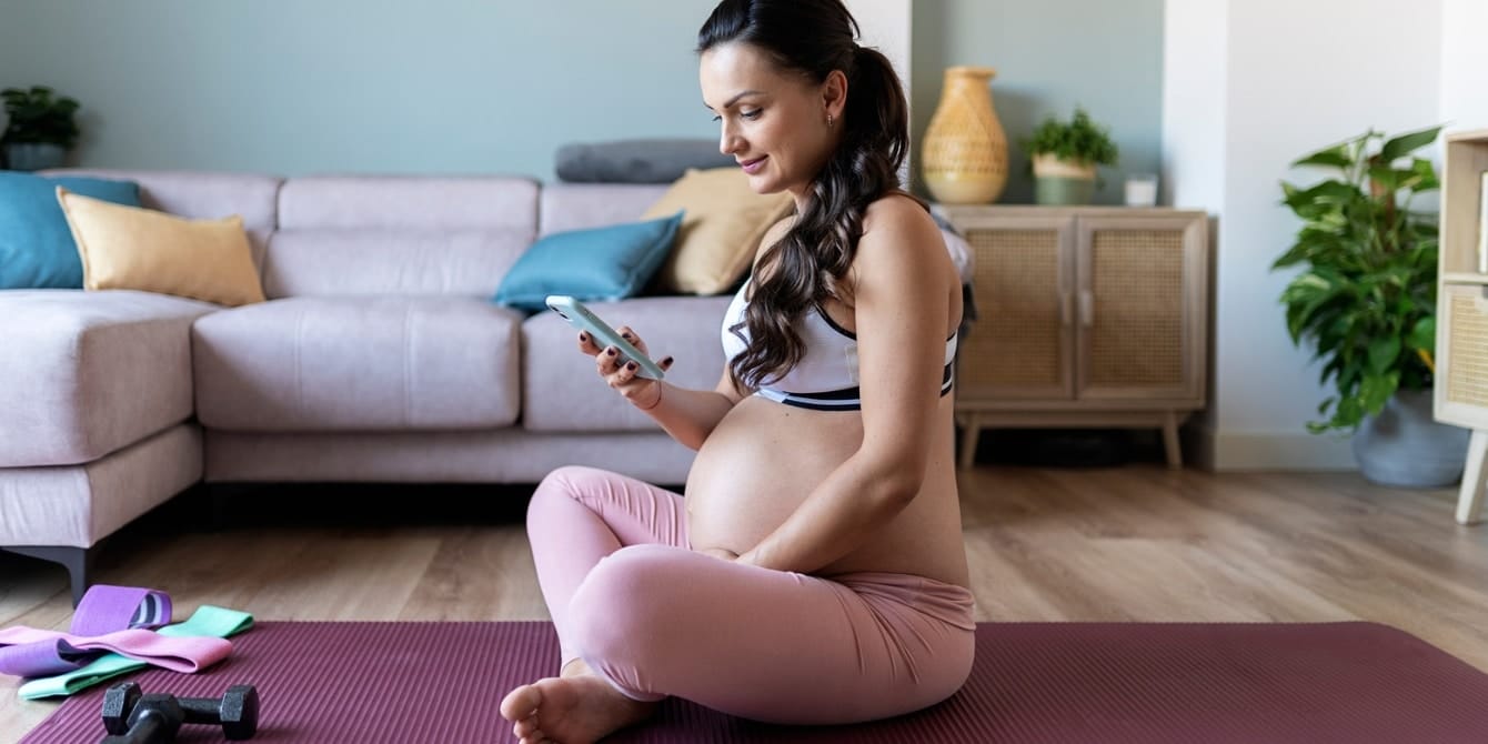 Working out while pregnant: The best pregnancy workout apps pregnant woman with phone on yoga mat - pregnancy workout apps