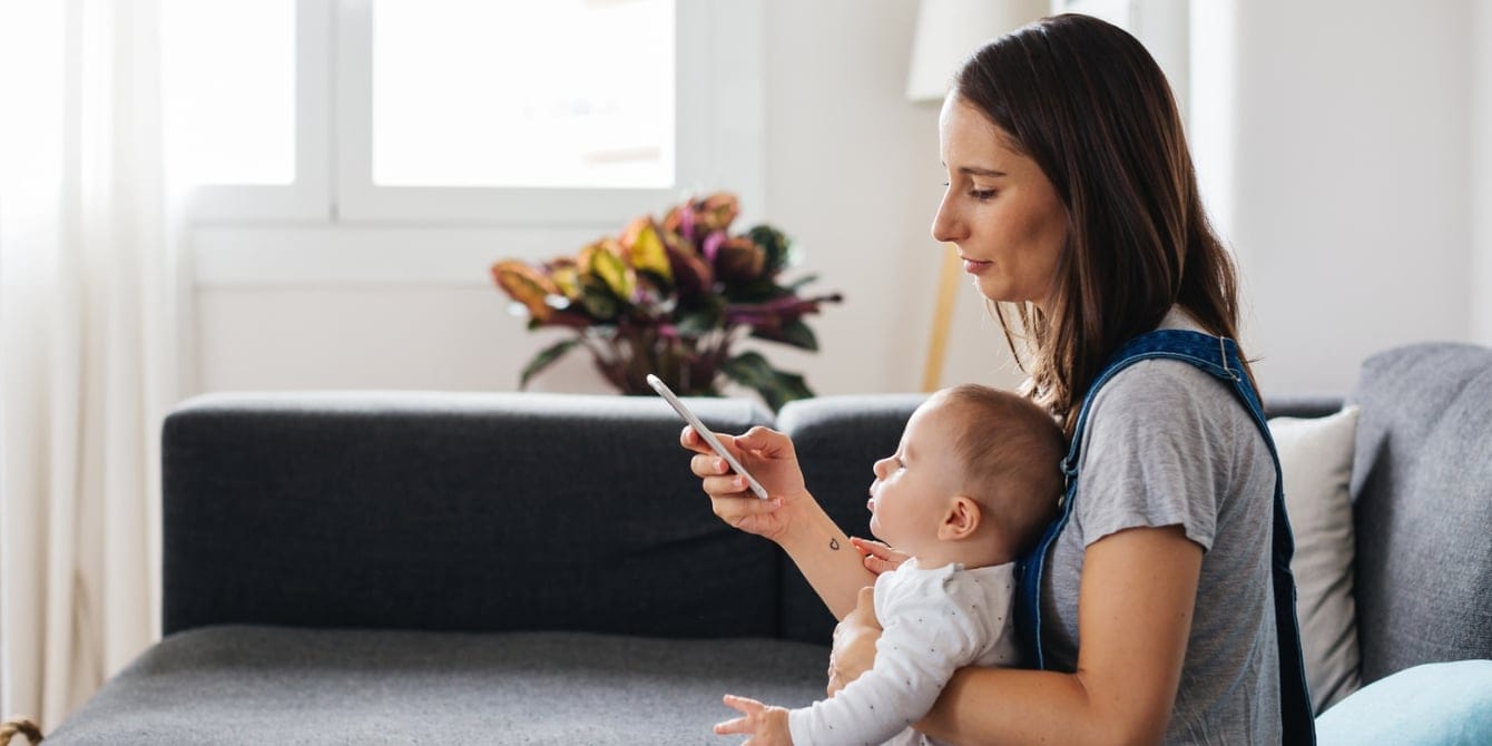 Can we please stop calling it ‘mom brain’? Young Mother Sitting With Her Baby Using Smartphone At Home - mom brain