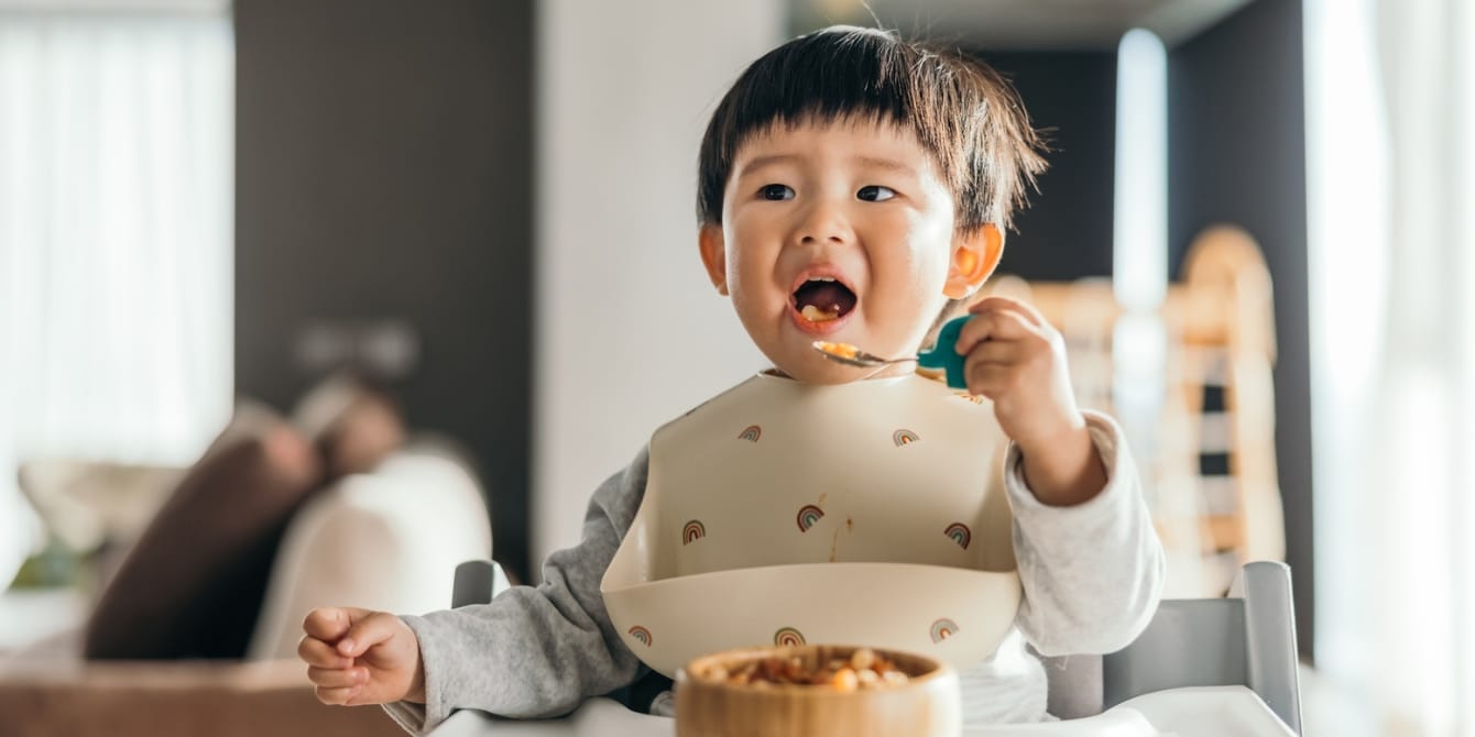 Should we really be worried about picky eaters? cute toddler asian boy wearing bib eating - picky eater guilt