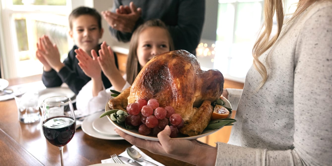 12 hacks for hosting Thanksgiving: A stress-free feast woman bringing thanksgiving turkey in to her family - thanksgiving hacks