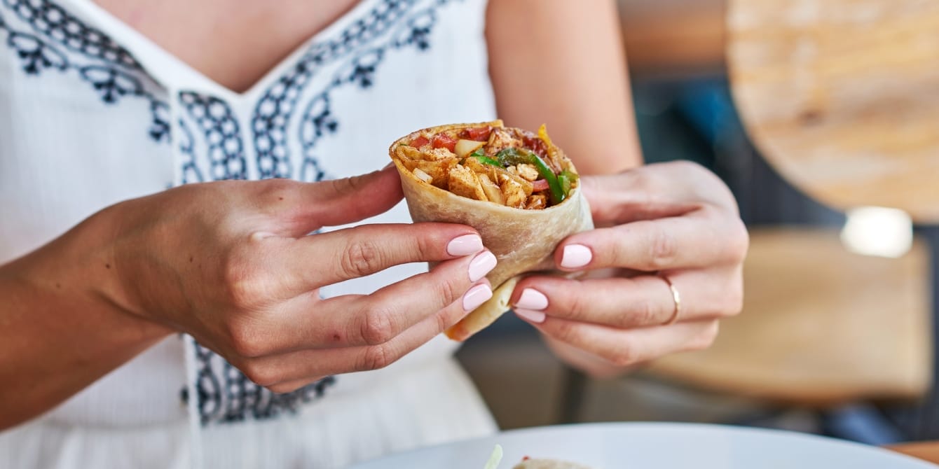 Swapping beef for chicken in your burrito can have big benefits for the environment, study shows close up woman holding a burrito dietary carbon footprint