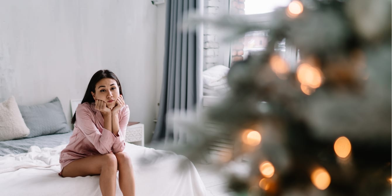 5 tips on surviving the holidays while struggling with infertility sad woman sitting on bed near Christmas tree infertility and the holidays