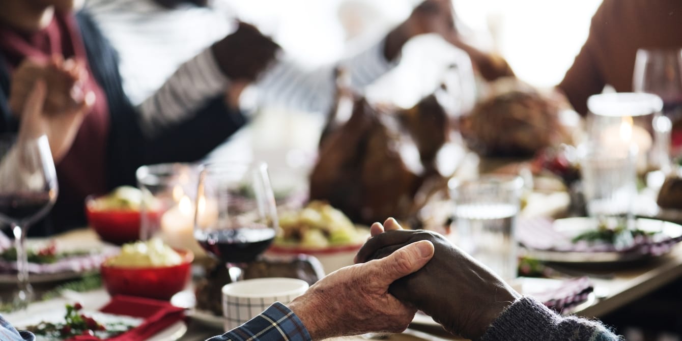 Facing opposing family values this holiday season family holding hands around dinner table breaking cultural traditions