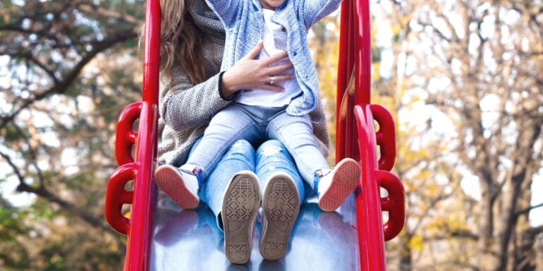 Did you know going down a slide with your toddler on your lap is actually unsafe? toddler on mothers lap on slide toddler fracture