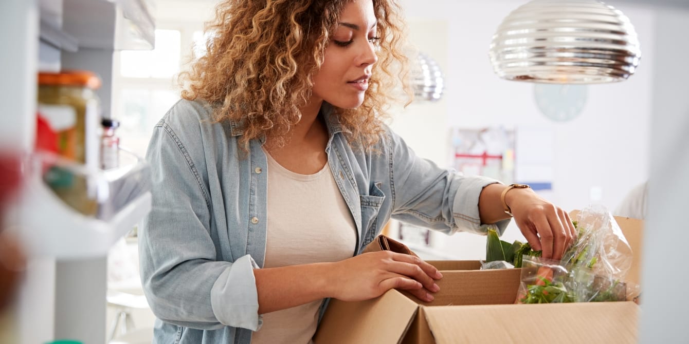 Your ultimate guide to postpartum meal-prep, according to a dietitian woman stocking fridge with food postpartum meal-prep
