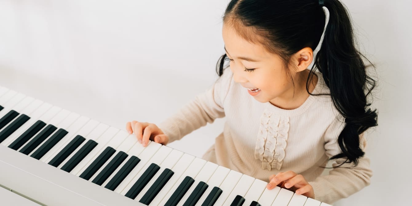 How to encourage your kid to practice their instrument, according to music education experts happy girl practicing piano - how to get your kid to practice music