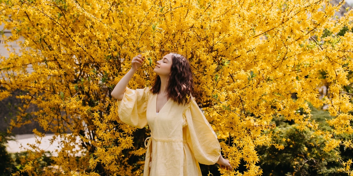 Spring’s yellow: A wistful season of beginnings and endings woman in yellow dress by forsythia flowers - mothering in a transitional season