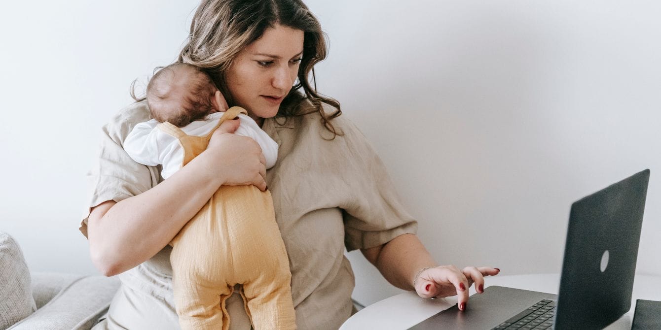 Childcare costs are impacting every aspect of moms’ lives mom holding baby while working - rising childcare costs
