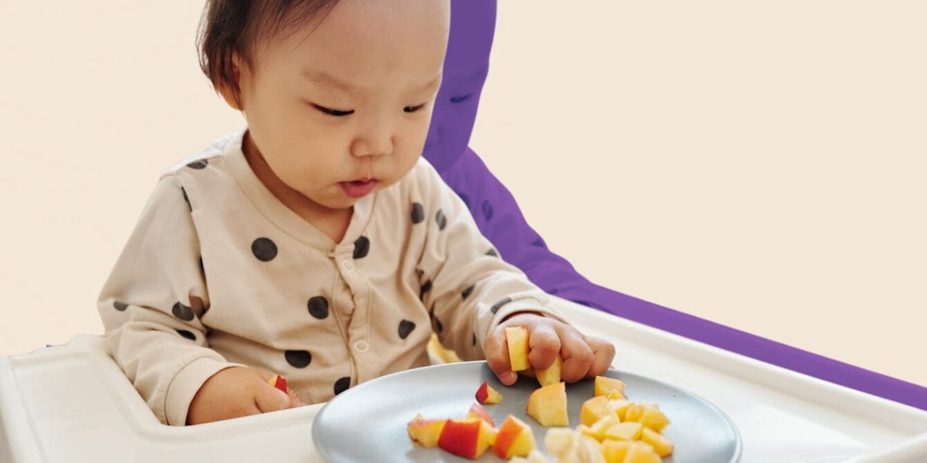 6 signs your baby’s feeding routine is working well Baby eating diced apple and diced cheese on a plate while sitting in high chair